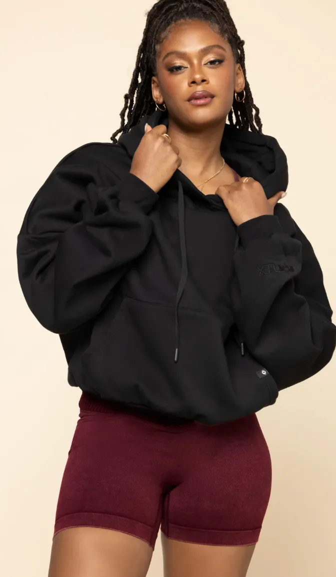 Model in an oversized black hoodie and burgundy bike shorts