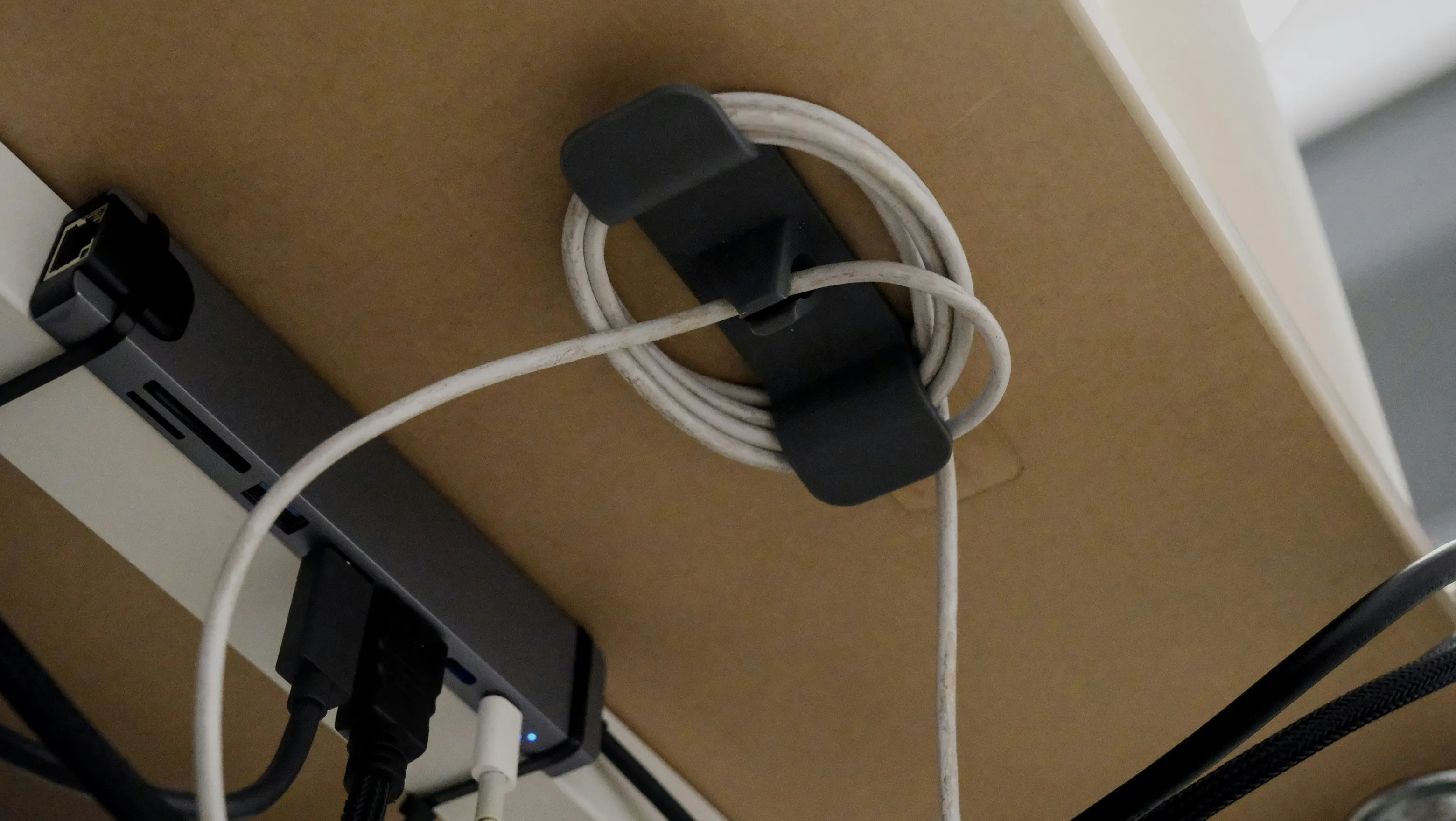 Coiled white cable held in a clip under a desk beside a USB hub