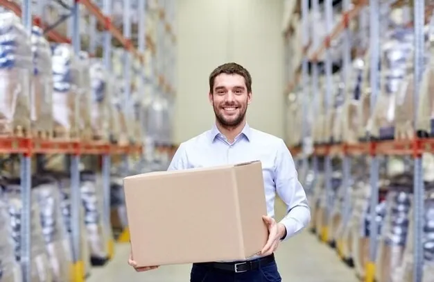 Smiling man holding a cardboard box in a warehouse aisle