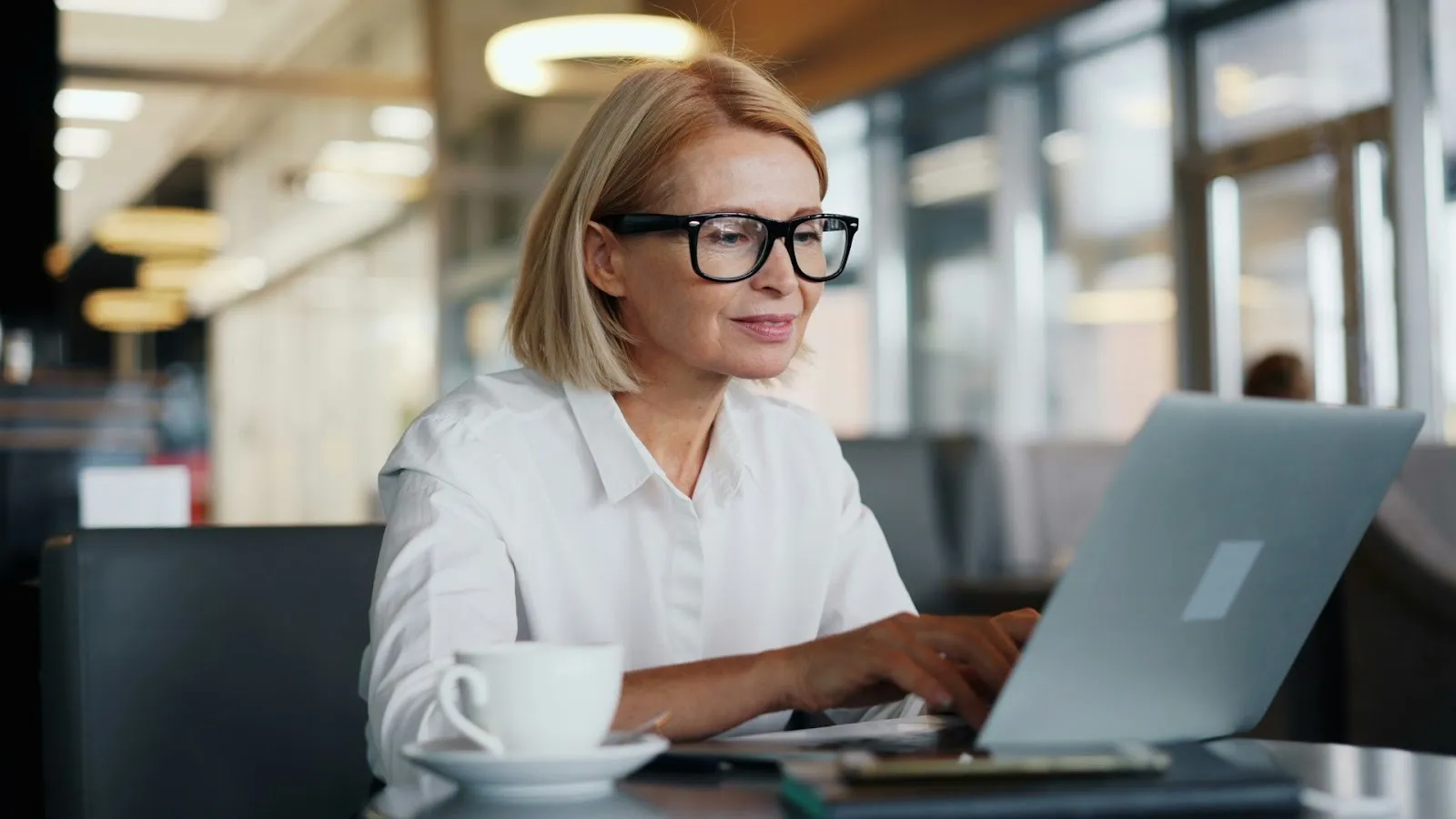Woman in glasses typing on a laptop at a café table