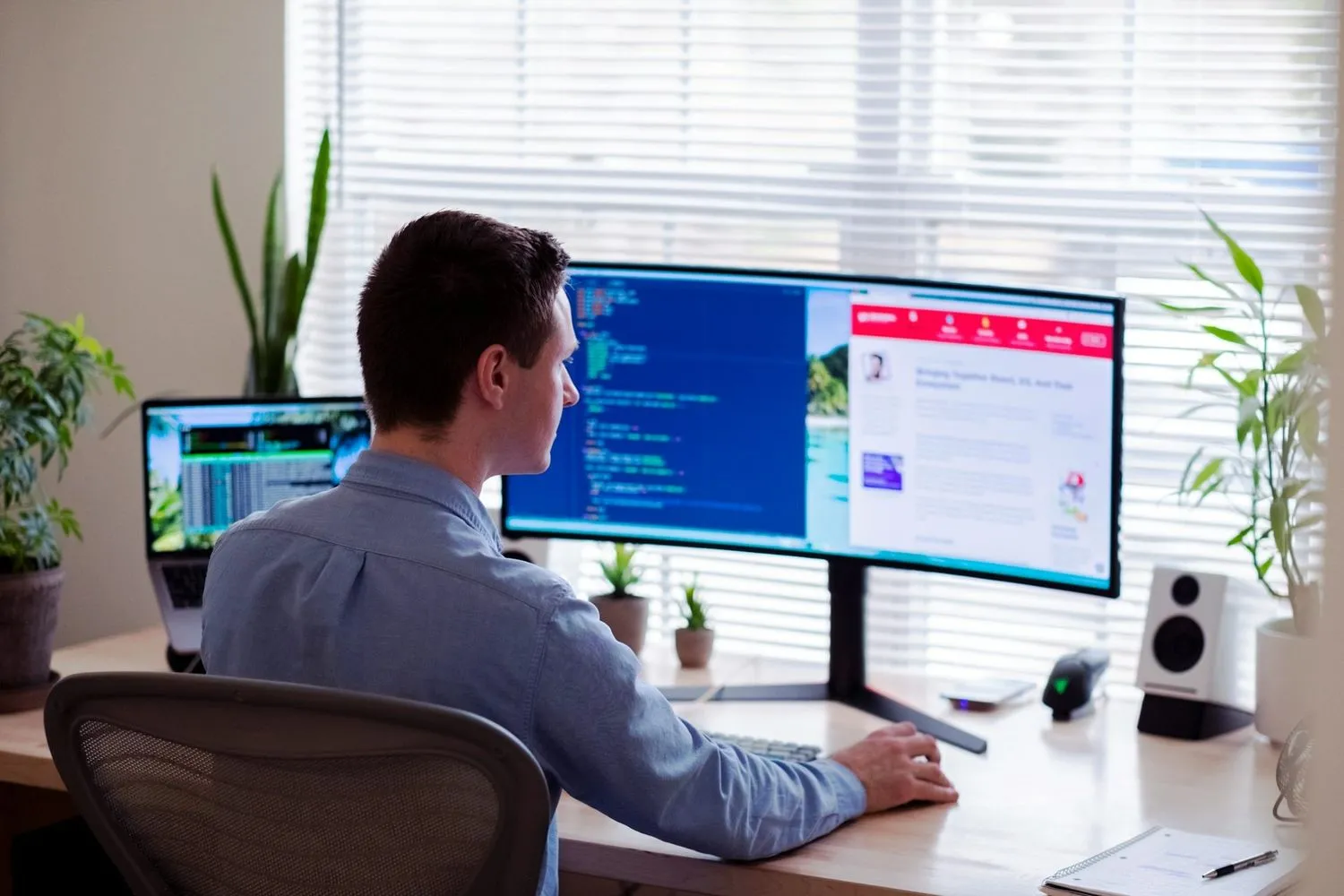 Man at a curved monitor with code on one side and a web page on the other