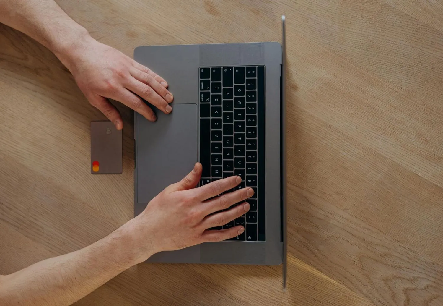 Hands on a laptop keyboard next to a payment card, seen from above