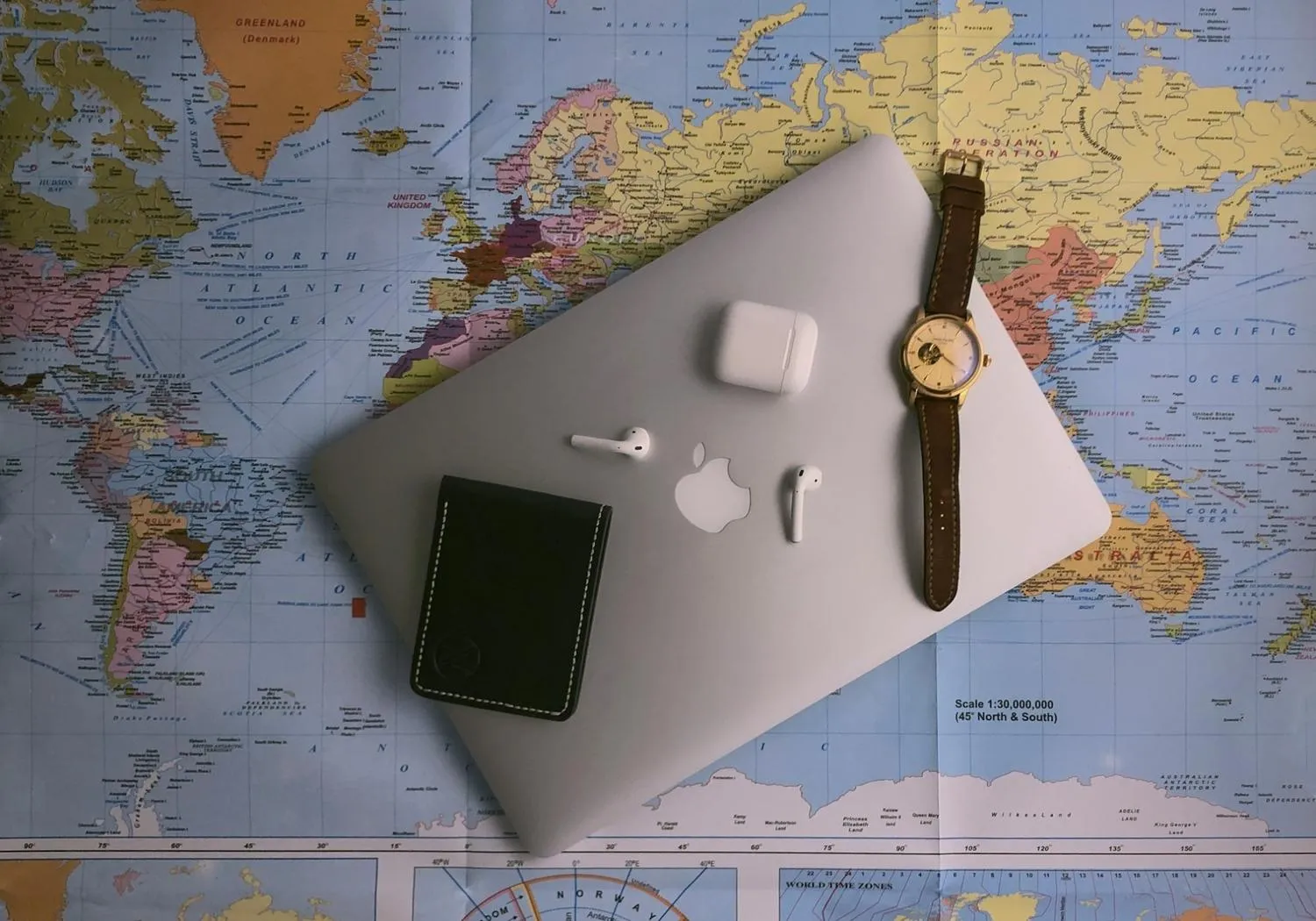 Laptop, wallet, watch, and earbuds laid on a world map