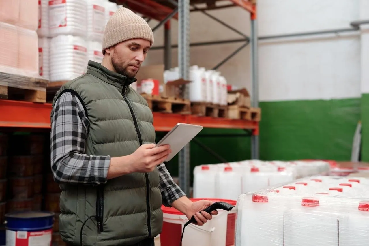 Warehouse worker checking a tablet and holding a barcode scanner beside pallets