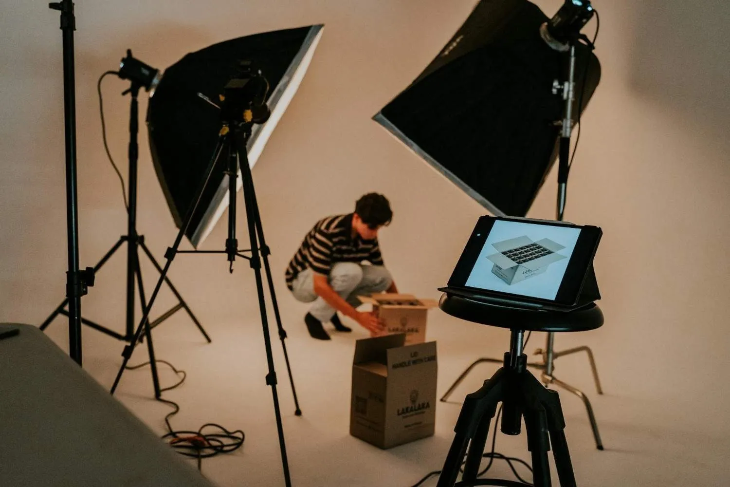 Photo studio with softbox lights, a camera on a tripod, and a person unpacking a box