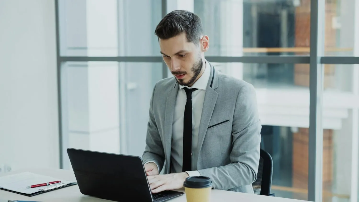 Man in a gray suit working on a laptop at an office desk