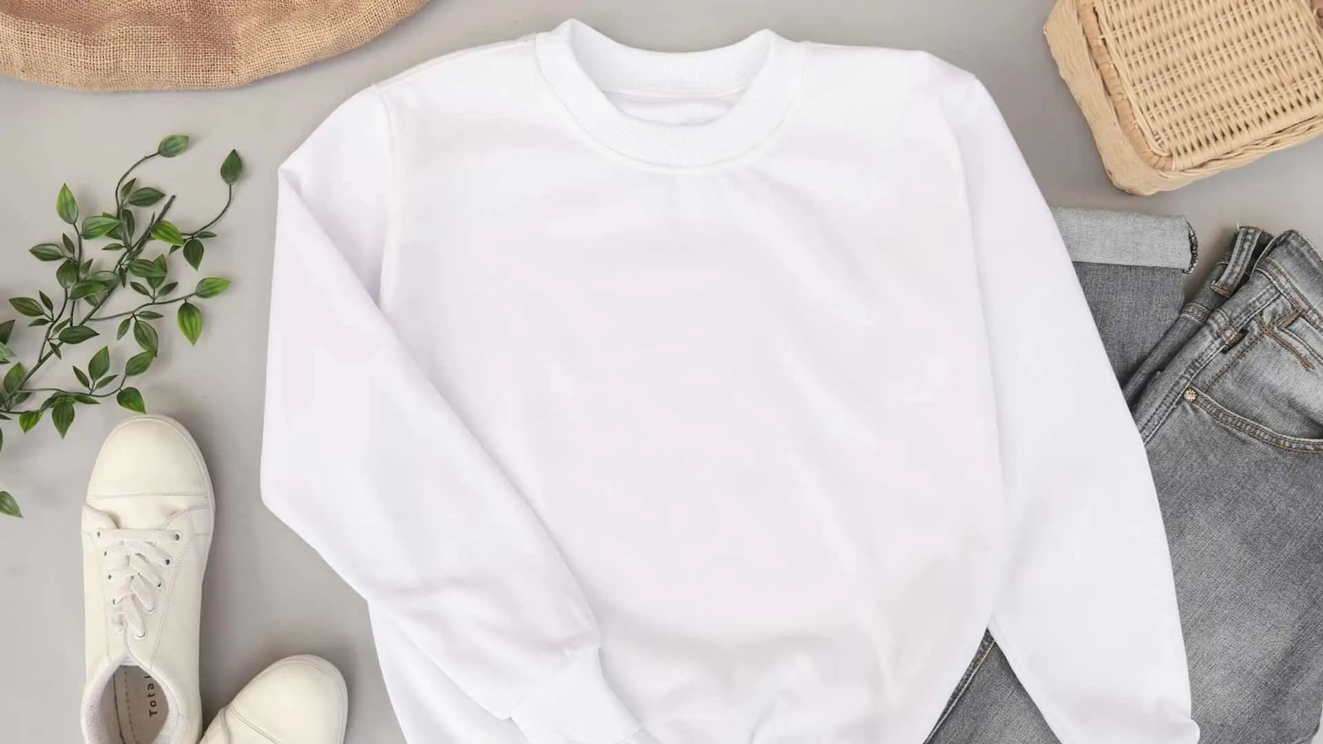 Blank white sweatshirt laid flat with jeans, white sneakers, and a wicker basket