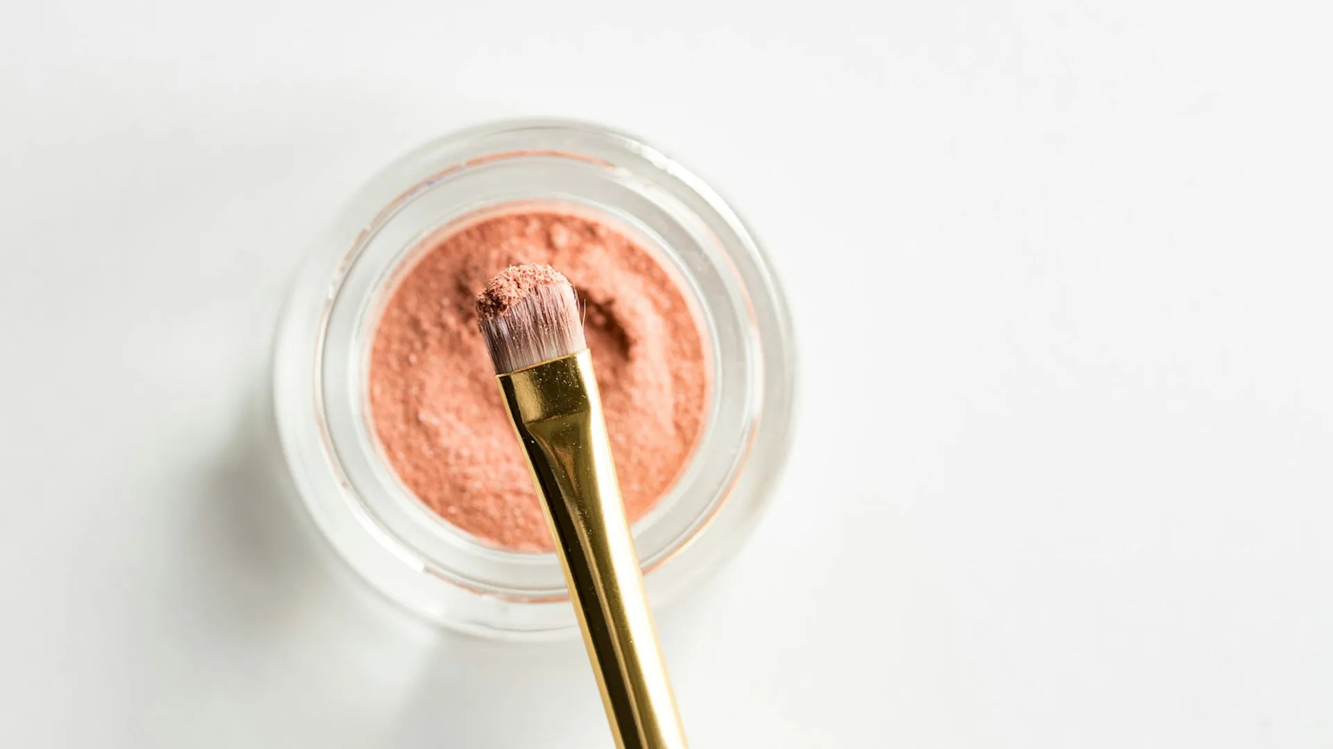 Makeup brush dipped in a jar of peach loose powder