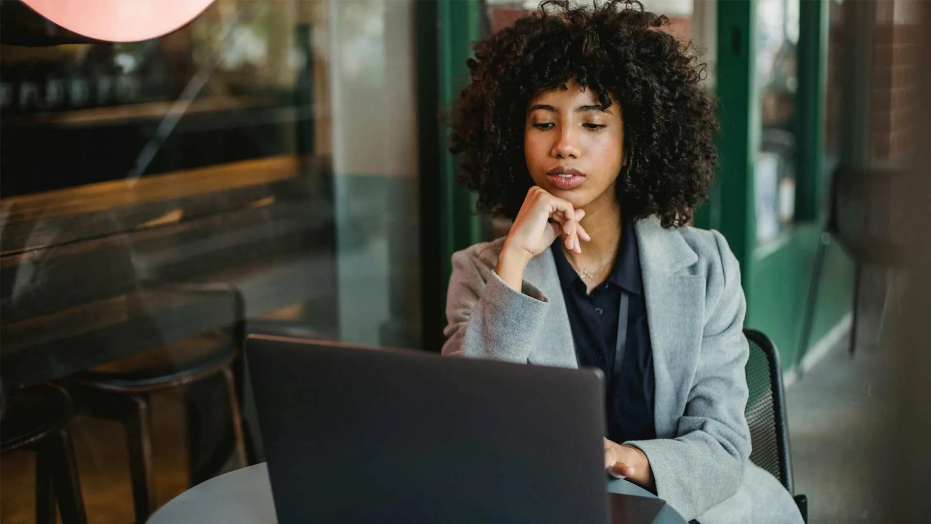 Woman in a gray blazer looking at a laptop in a cafe